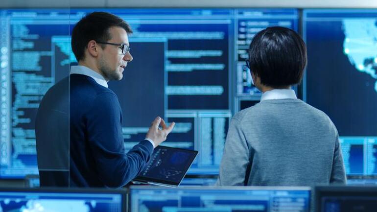 System Security Specialist Working at System Control Center. Room is Full of Screens Displaying Various Information.